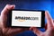 Hands holding smartphone displaying logo of Amazon