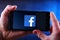 Hands holding smartphone displaying logo of Facebook