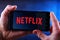 Hands holding smartphone displaying logo of Netflix