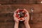 Hands holding strawberries with yogurt chocolate pumpkin seeds chia sunflower seeds and apple in a white bowl on a wooden table