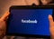 Hands holding tablet with Facebook logo on a black screen