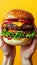 Hands holding a tasty burger on a bright yellow background, delicious fast food concept