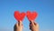Hands holding two red heart-shaped recycled cardboard on blue sky background. Love symbol for valentines day. Concepts of Love and