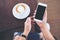 Hands holding white mobile phone with blank black screen with coffee cup on wooden table and floor background