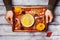 Hands holding wooden tray with autumn pumpkin soup decorated seeds and thyme in white bowl on rustic table top view.