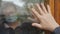 Hands of hope. An elderly man and woman touch the palms of their hands through the glass window that separates them from