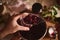 Hands of a housewife holding a sterilized glass jar and filling it with homemade freshly brewed cherry berry jam over a saucepan