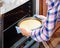 Hands of housewife taking cheesecake out of oven in kitchen