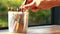 Hands keep colored pencils in a plastic round box placed on a wooden table by the window with the sun shining on green nature boke