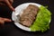 Hands with knife and fork sliced pork meat with lettuce leaves on a plate