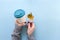 Hands in long sleeve knitted sweater, holding bamboo reusable cup and autumn leaf, overhead on blue background