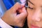 Hands of makeup artist glue artificial eyelashes to girl model, face closeup.