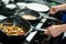 Hands of male chef roasting piece of salmon and vegetable stew on frying pans