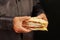 Hands of man in a black shirt are holding a double sandwich on black background