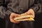 Hands of man in a black shirt are holding a sandwich on black background close up