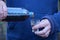 hands of a man in blue clothes holding a glass glass and a plastic bottle pouring a black drink