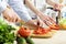 Hands of man chopped red bell pepper on board. Couple chopping vegetables in kitchen