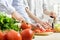 Hands of man chopped red bell pepper on board. Couple chopping vegetables in kitchen