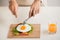 Hands of man cut the eggs on cutting board, served with bread, herbs, sausage and fresh juice