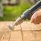 Hands man with electrical rotating brush metal disk sanding a piece of wood