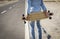 Hands of man holding skateboard on road. Rear view of man wearing denim clothes holding skateboard on rural road. Sportsman