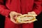 Hands of man in a red shirt are holding a double sandwich on black background