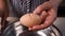 Hands and a metal steel knife breaks a brown chicken egg and the yolk falls into a metal pan. Close-up.
