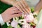 Hands of newlyweds on the background of wedding bouquet. Gold wedding rings on the finger of bride and groom, close-up. Concept