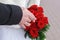 Hands of newlyweds with a red roses bouquet.