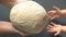 The hands of an old woman transmit bread dough to the small hands of a girl. The intergenerational connection.