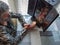 Hands of an older woman praying with her hands linked to a niche with a statue of Jesus and a candle