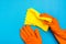 Hands in orange rubber gloves hold a yellow microfiber rag on a blue background. The concept of protecting the skin of the hands