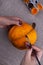 Hands paint a homemade papier mache pumpkin in orange on a burlap background