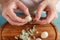 Hands peel boiled quail eggs from shell under wooden cutting board, close-up.