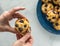 Hands peeling back the paper liner of a freshly made blueberry muffin.