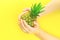 Hands with pineapple on summer neon yellow background