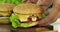 Hands placing cheese burger on a wooden tray.