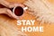 Hands placing cup of tea next to stay home message laid on an orange surface