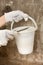 Hands of plasterer holding bucket with plaster and spatula