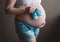 Hands of a pregnant girl hold belly and small baby booties, awaiting the birth of a baby