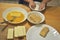 Hands of a preschooler is coating slices of cheese in eggs, flour and breadcrumbs