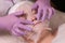 The hands of a professional cosmetologist in lilac gloves impose a nourishing mask on the patient. Cosmetic mask on a woman`s fac