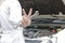 Hands of professional young mechanic man holding wrench and raising two fingers up it is shows fight with job against car in open