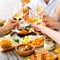 Hands with red wine toasting over served table with food.