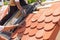 Hands of roofer laying tile on the roof. Installing natural red tile. Roof with mansard windows