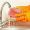 Hands in rubber gloves with sponge wash glass under running water