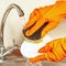 Hands in rubber gloves with sponge wash plate under running water