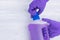 Hands in rubber purple gloves open a bottle of liquid floor cleaner on a light background