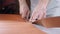 Hands of skilled leather craftsman using plastic pattern and leather knife to cut out part from piece of red leather