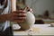 Hands of skilled woman making white vase from clay standing at dirty table